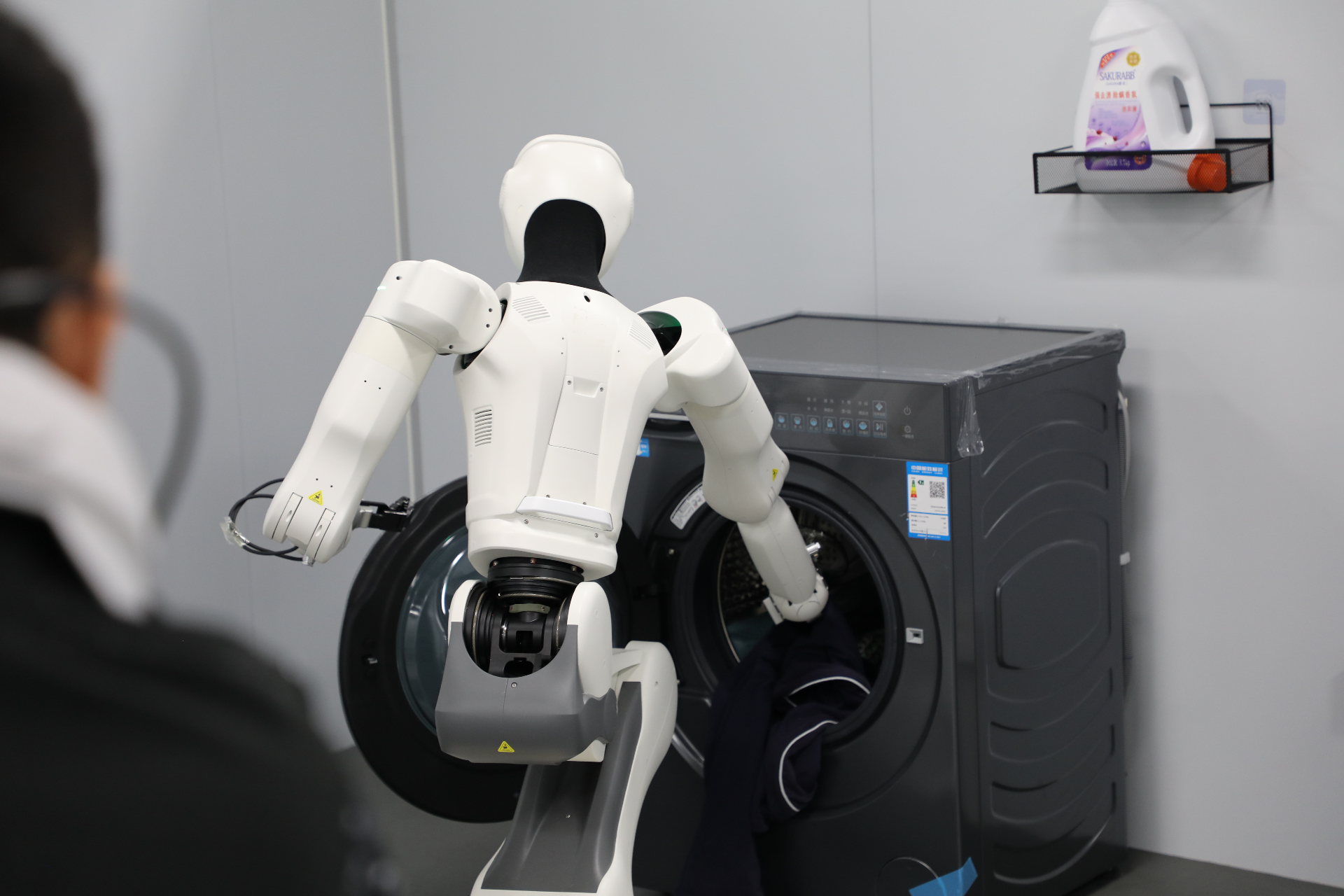 Humanoid robot loading laundry into a washing machine